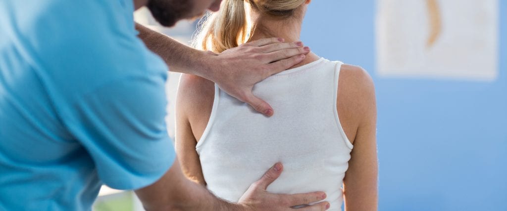 Male physiotherapist giving back massage to female patient in clinic